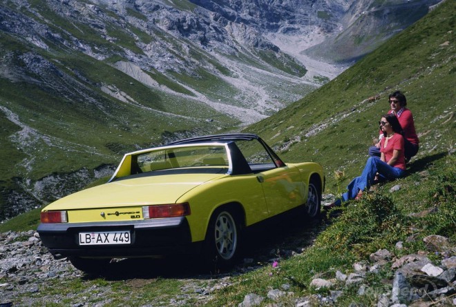 A yellow Porsche 914 in front of a mountain landscape