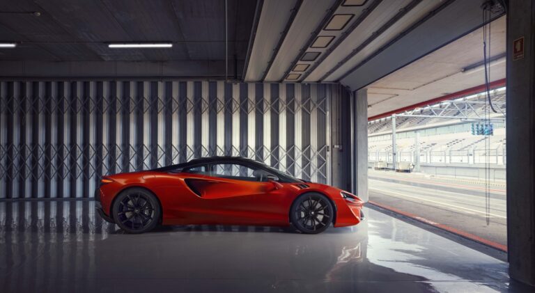 Vermillion red 2022 McLaren Artura in a garage at a racetrack. Buy a McLaren with #pfs_leasing