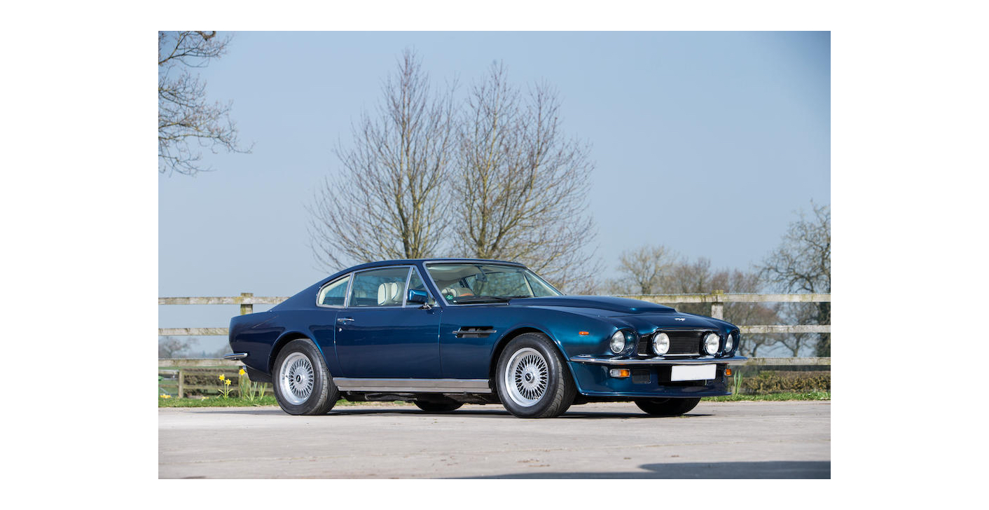 Slate Blue Metallic 1976 Aston Martin V8 Saloon parked in front of a fence and daffodils. Aston Financing with the PFS Simple Lease. #007