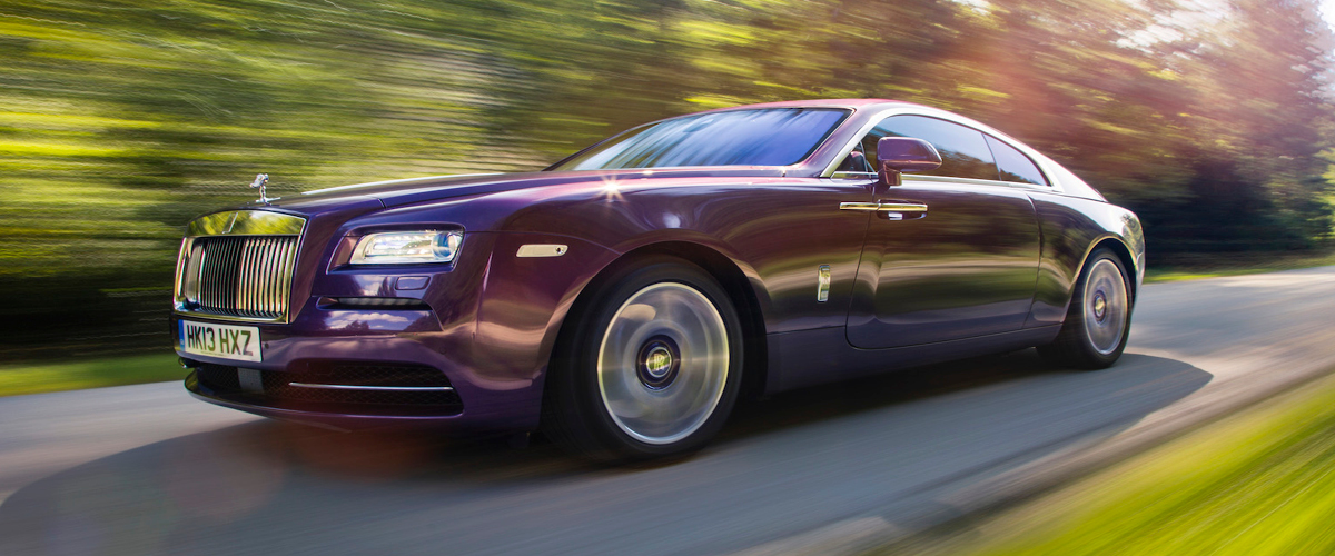 Front left view of Rolls-Royce Wraith, night. Purple Rolls-Royce, Speeding down road with green blur. Premier's Simple Lease makes driving a Rolls-Royce possible.