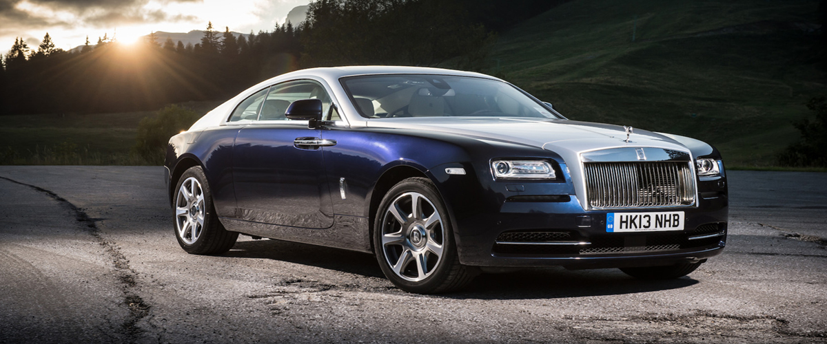 Front left view of Rolls-Royce Wraith, sunrise over pine trees. Silver and Blue two-door.Rolls-Royce Loan