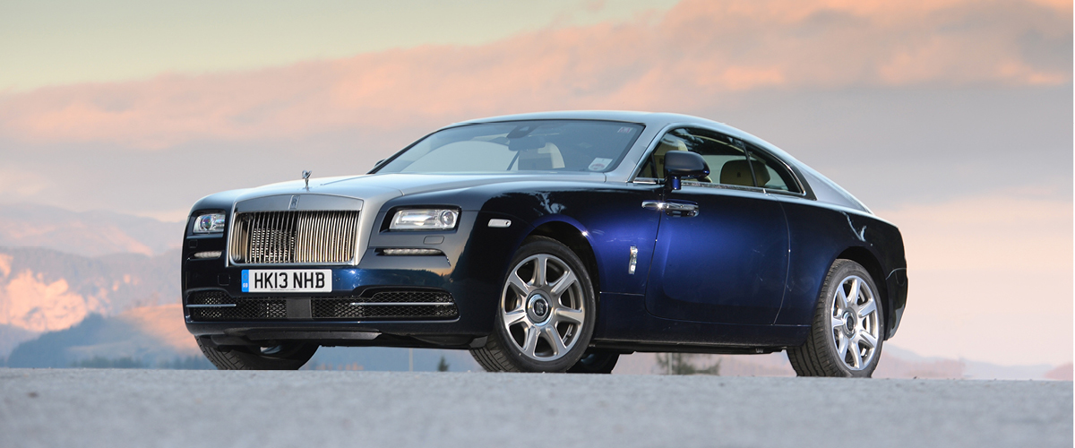 Front left view of Rolls-Royce Wraith, day. Blue and silver coupe. Mountain skyline. Rolls-Royce Financing