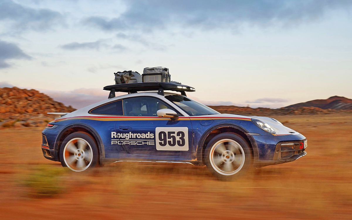 Blue and white 2023 Porsche 911 Dakar driving in desert, right side view