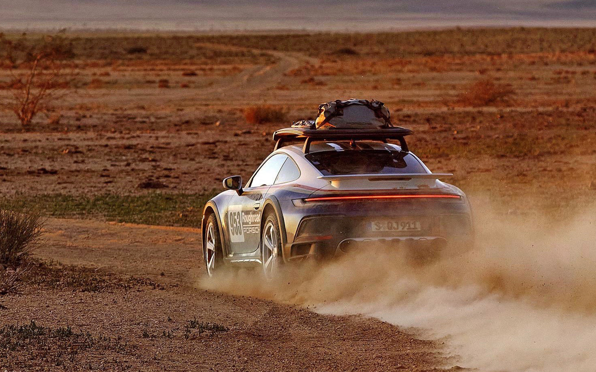 Blue and white 2023 Porsche 911 Dakar driving in desert, rear view