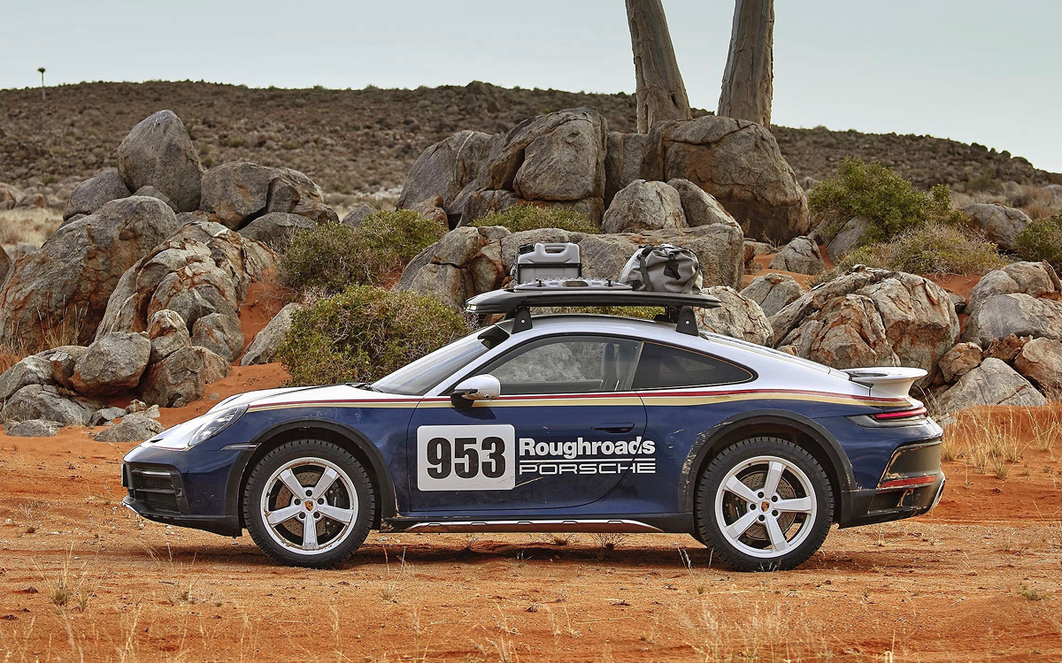 Blue and white 2023 Porsche 911 Dakar driving in desert, left side view