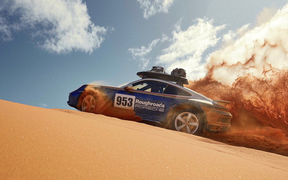 Blue and white 2023 Porsche 911 Dakar driving on sand dune, low view